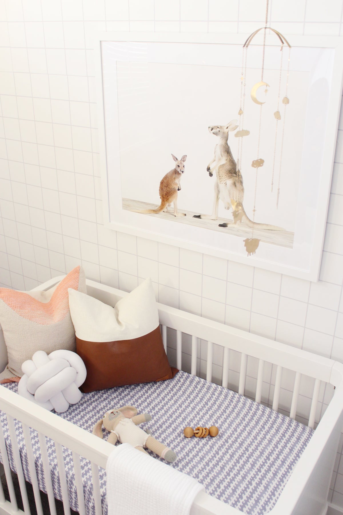 Brass Counting Baby Sheep Mobile hanging over a white crib in a styled modern nursery, beside kangaroo wall art - Ariana Ost