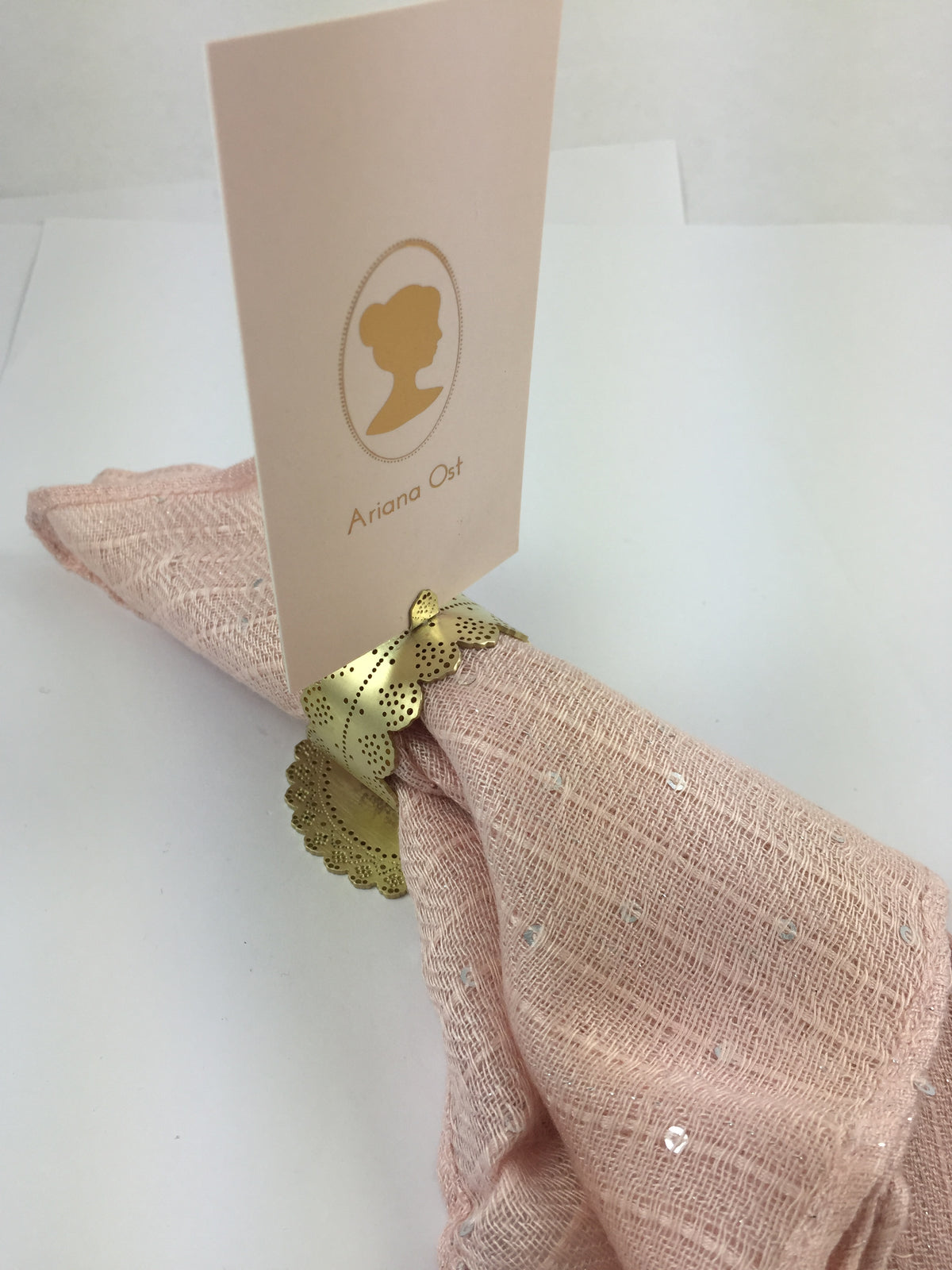 Gold Lace Doily Place Card Holder holding a card and a blush linen napkin at once, on its scalloped doily base - Ariana Ost