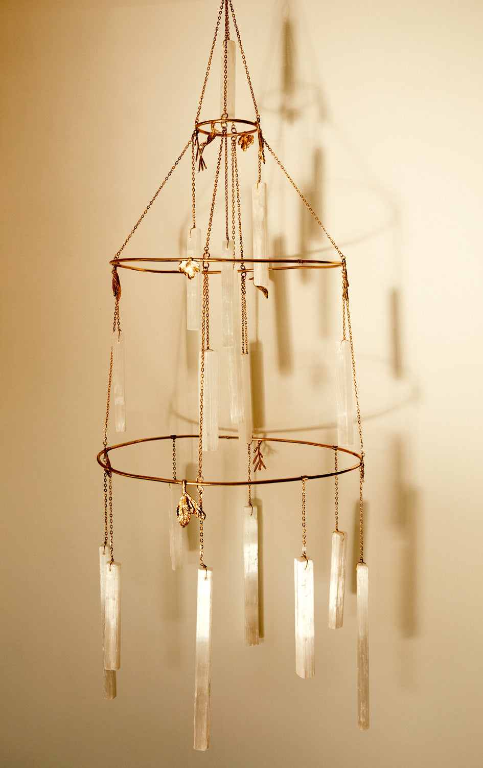 Selenite Crystal Chandelier glowing in warm sunlight, casting long shadows on the wall - Ariana Ost