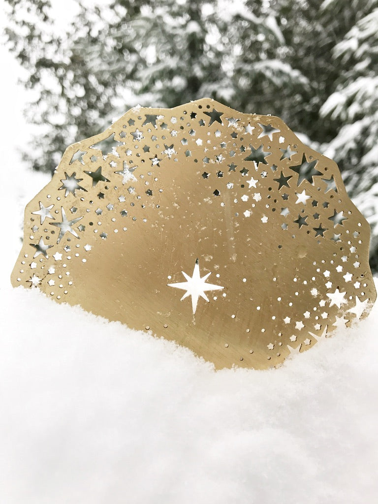 Gold Celestial Coaster standing in fresh snow against snowy pine trees, its laser-cut stars catching the winter light - Ariana Ost
