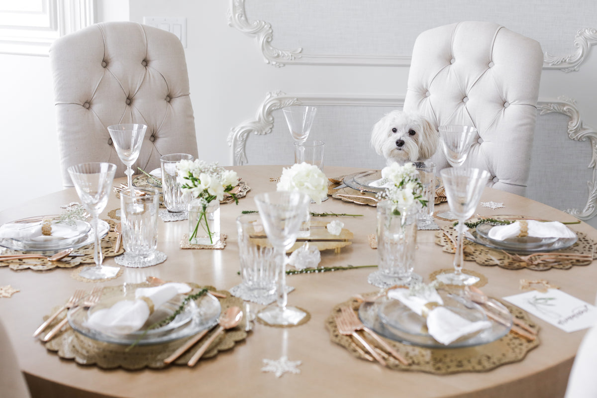 Dinner party tablescape with gold laser-cut doily chargers and coasters, crystal glassware and tufted chairs - Ariana Ost