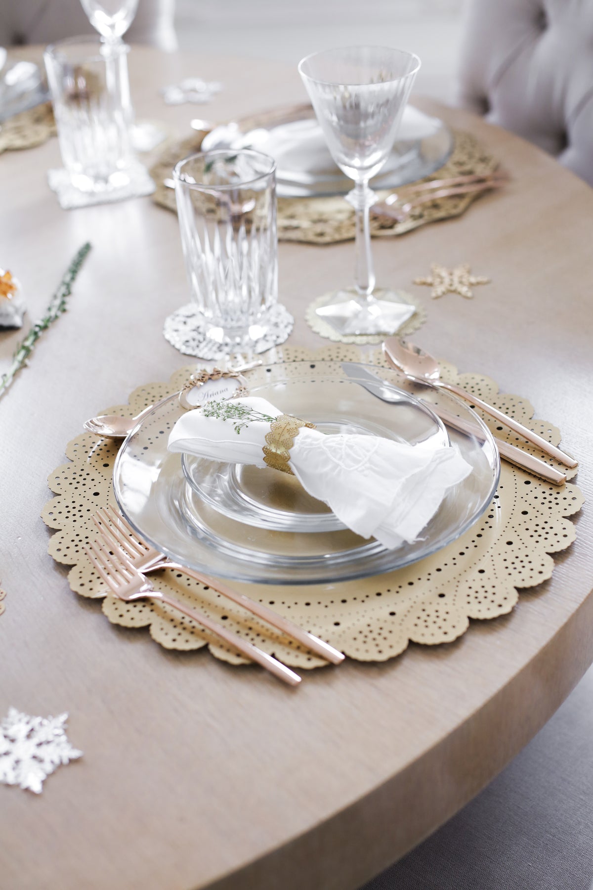 Place setting on a gold Lace Doily Charger with crystal glassware, rose gold flatware and winter greenery - Ariana Ost